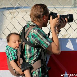 Portrait of an unknown photographer shooting races at the Toyota Grand Prix at Long Beach while his child is sound asleep in the midst of all the engine noise.