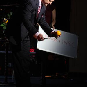 Magicially transforming a borrowed dollar bill from a spectator's pocket inside of an orange. On stage performing at the 2011 Salute To Magic in New York City.