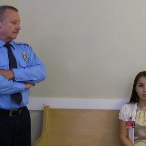 The officer (Larry Hicks) watches Kayla Butler (Jacqueline Peter) as she waits to be processed into the Lost Sheep Addiction Centre.