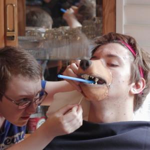 Morgana McKenzie applying a prosthetic appliance on Connor Adsett for the production We All Go the Same
