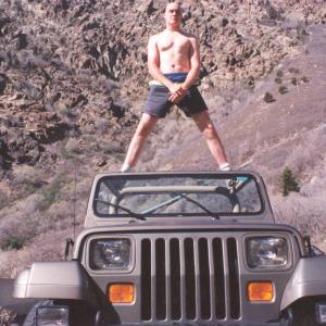 Hawke bald and shirtless in shorts standing on top of Leif's Jeep in Cottonwood Canyon, Utah.