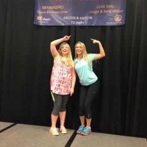 Kirsten and sister Kaitlyn Hoge pose under poster with their names listed after hosting an LPE event in St Louis