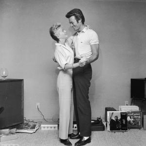 Clint Eastwood and his first wife Maggie dance next to a turntable and a rack full of records in a living room in 1965