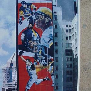In August of 1992, I was hired by Ambassador Signs to paint a Sports Mural designed by Judy Penzer. assisted by Robert Harmon, the 46' by 135' mural took us 4 weeks. It started at the top of a 26 story building in downtown Pittsburgh. The mural was eleven stories high.